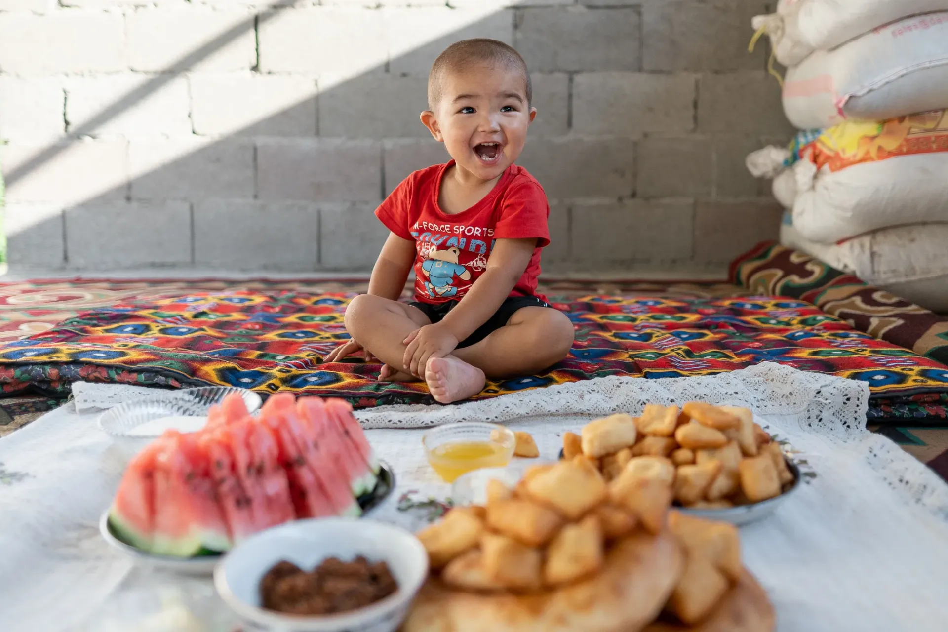 Ariet, 2 years old, sits on the floor with some of his favourite foods, at home in Kurshab village, Osh Oblast, Kyrgyzstan